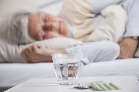 Une femme âgée qui dort avec des médicaments sur une table devant elle 