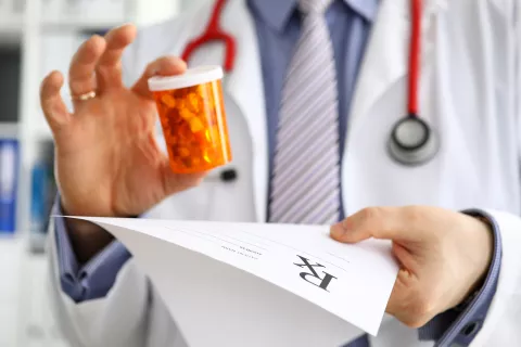 édecin tenant une boite de médicaments et une prescription