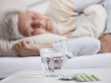 Une femme âgée qui dort avec des médicaments sur une table devant elle 